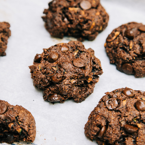 A 3/4 angle shot of chocolate zucchini muffin tops on a white parchment background.