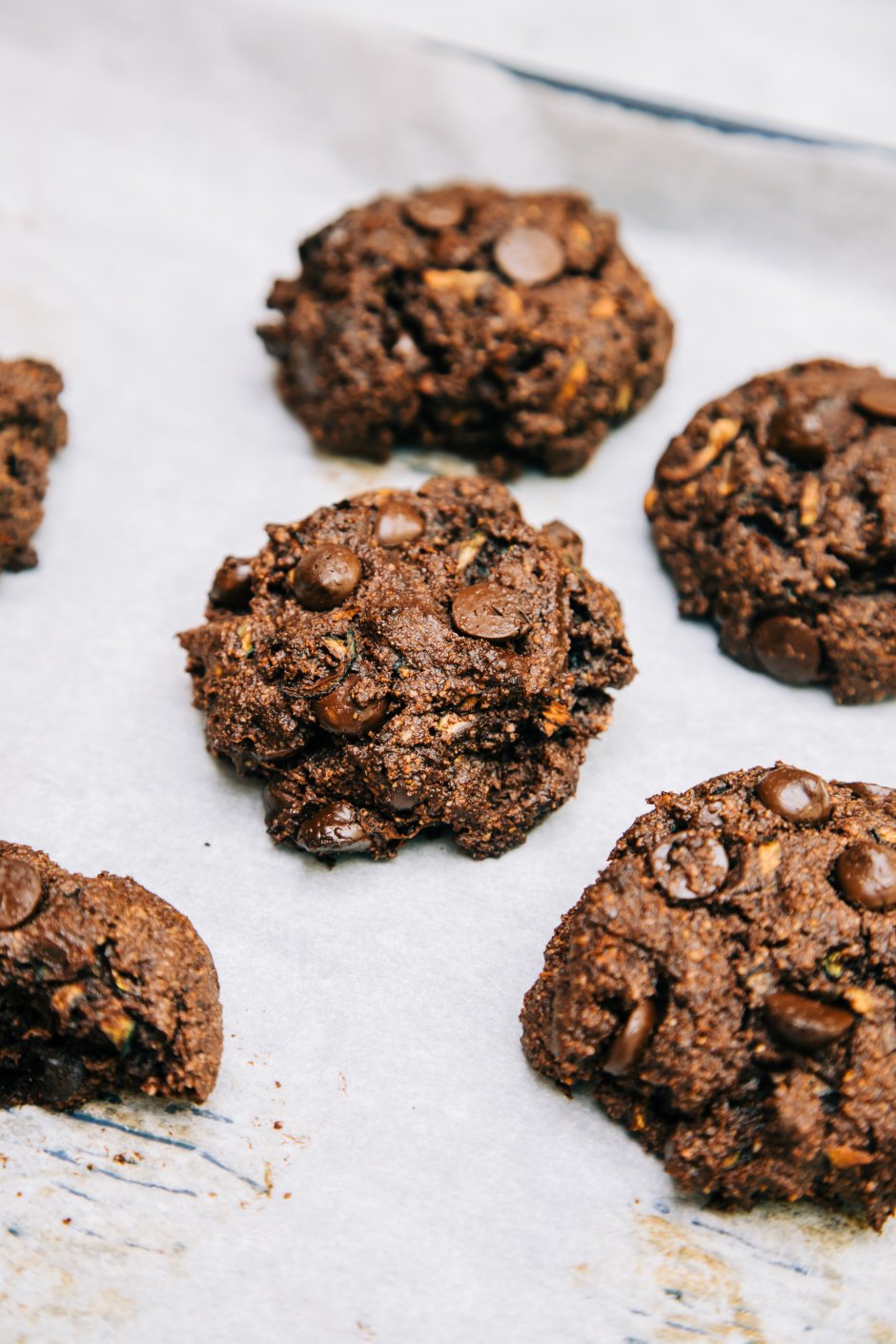 A 3/4 angle shot of chocolate zucchini muffin tops on a white parchment background.