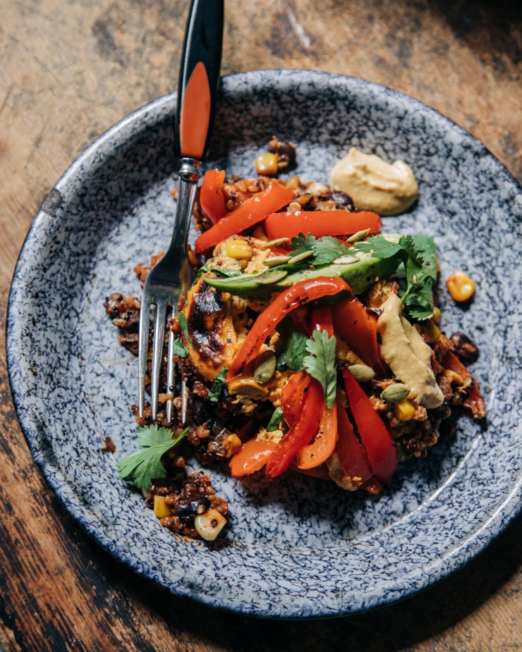 An overhead shot of a serving of a mixed quinoa, bell pepper, black bean, and corn dish. The serving is topped with a slice of avocado and chopped cilantro.