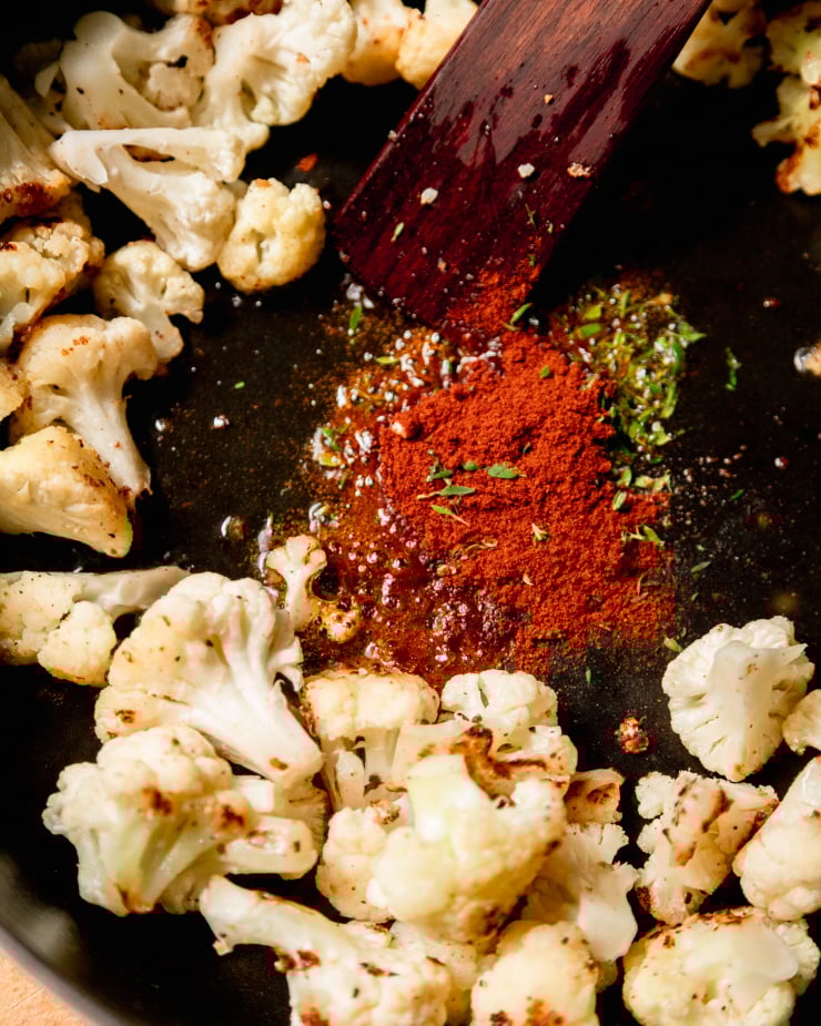 An up close shot of smoked paprika and thyme sizzling in hot oil, surrounded by cauliflower.