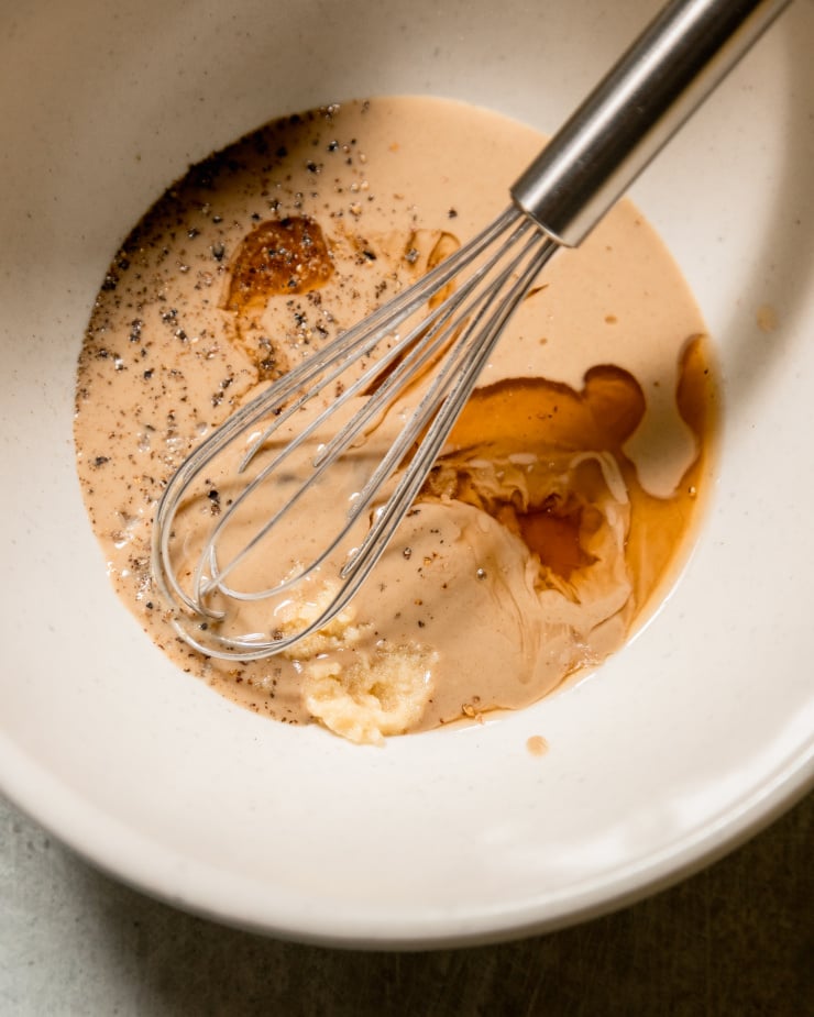 An up close shot of tahini sauce ingredients in a white bowl, before being whisked together.