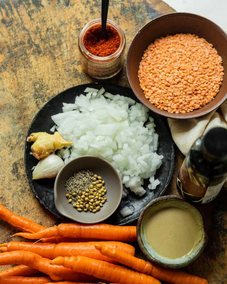 An overhead shot of ingredients for a spicy sesame carrot soup on a wood background.