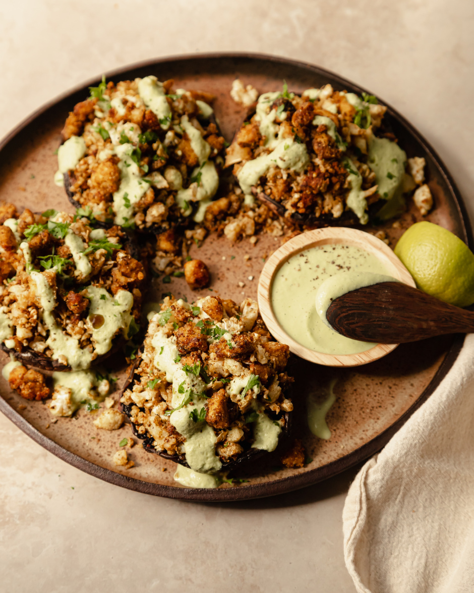A 3/4 angle shot of some stuffed portobello mushrooms drizzled with a pale green sauce on top of a speckled brown plate.