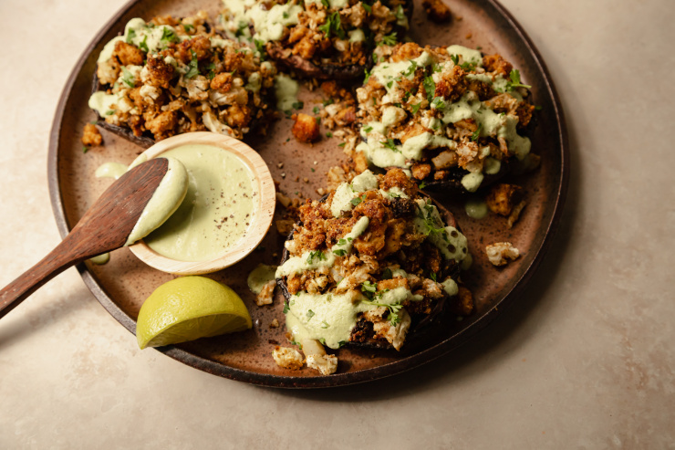 A 3/4 angle shot of some stuffed portobello mushrooms drizzled with a pale green sauce on top of a speckled brown plate.