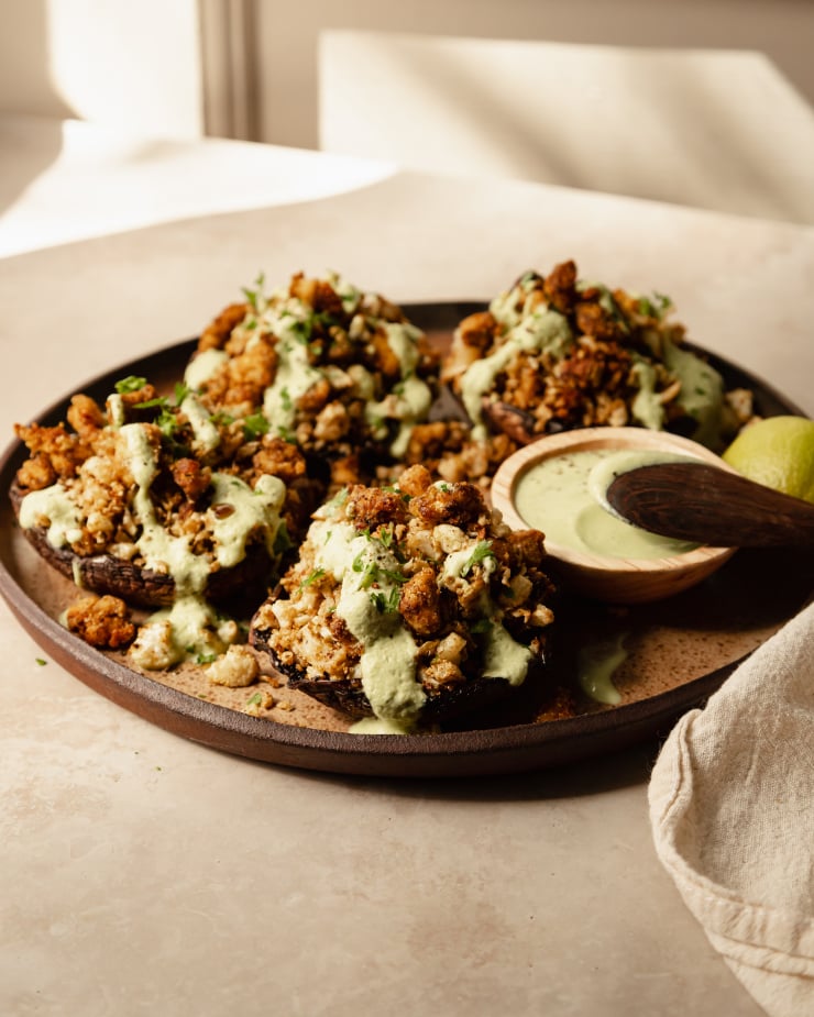 A 3/4 angle shot of some stuffed portobello mushrooms drizzled with a pale green sauce on top of a speckled brown plate.