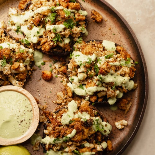 An overhead shot of some stuffed portobello mushrooms drizzled with a pale green sauce on top of a speckled brown plate.