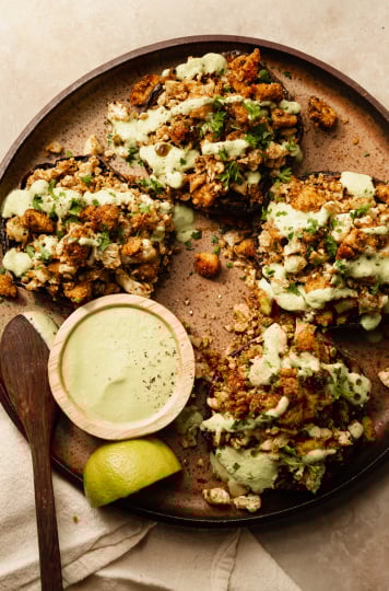 An overhead shot of some stuffed portobello mushrooms drizzled with a pale green sauce on top of a speckled brown plate.