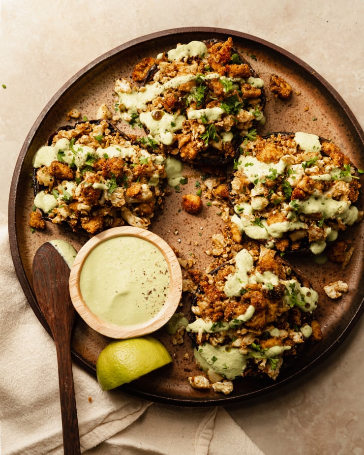 An overhead shot of some stuffed portobello mushrooms drizzled with a pale green sauce on top of a speckled brown plate.