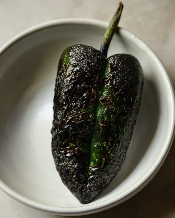 An up close shot of a charred poblano pepper in a white bowl.