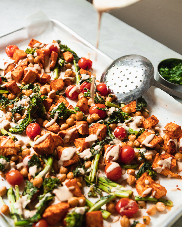 A 3/4 angle shot of peanut sauce being poured over roasted vegetables and chickpeas.