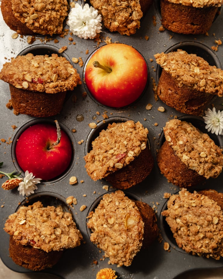 An overhead shot of baked vegan apple crisp muffins set upright in a muffin tin with apples in some of the muffin cups.