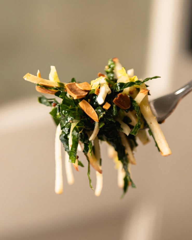 Image is an up close shot of a forkful of apple kale salad with toasted almonds.