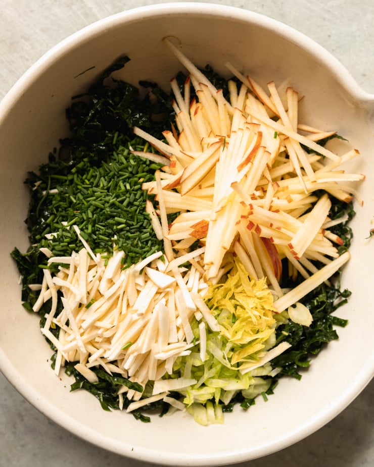 An overhead shot of finely sliced vegetables and fruit in a cream-coloured mixing bowl.