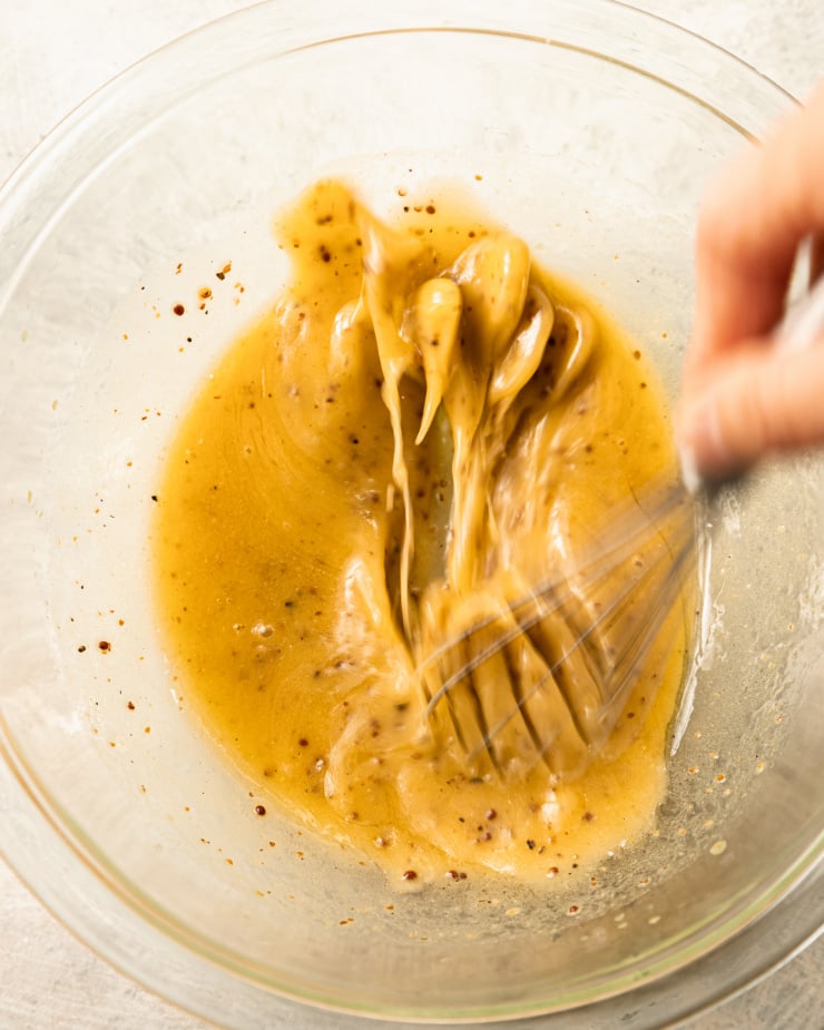 Image shows a hand quickly whisking a pale yellow vinaigrette.