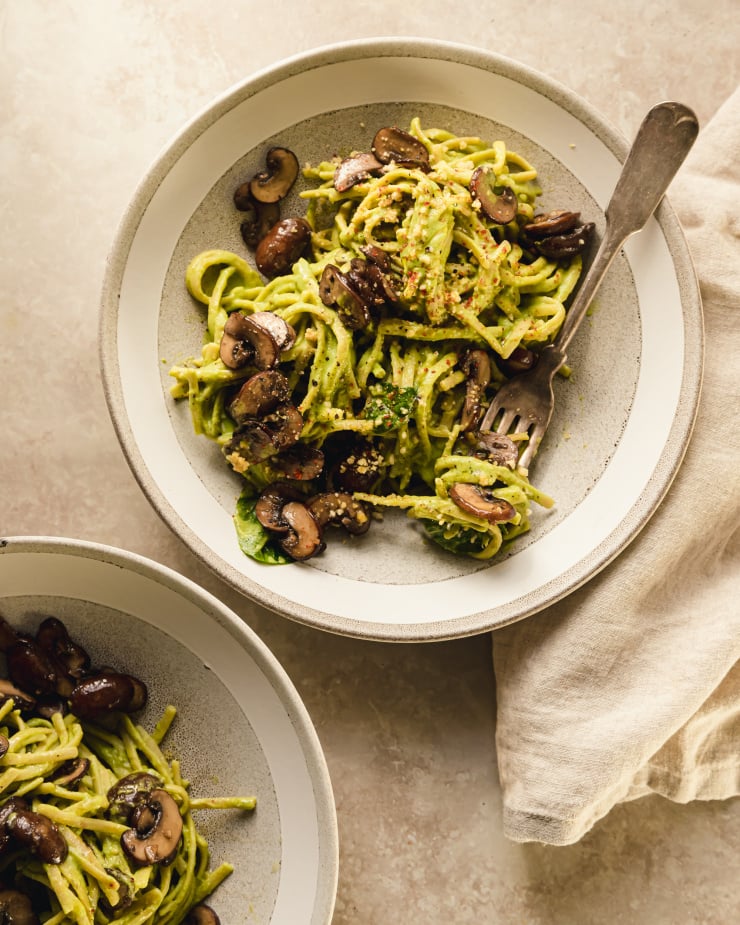 An overhead shot of one serving creamy vegan spinach and mushroom pasta in a light grey bowl.