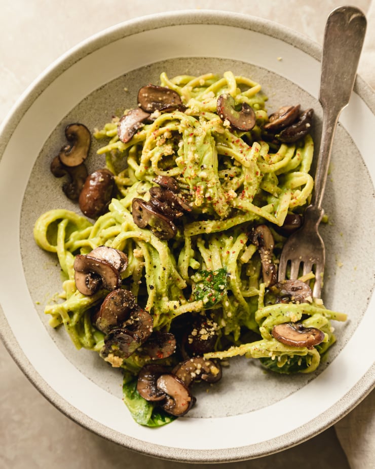 An overhead shot of a serving creamy vegan spinach and mushroom pasta in a light grey bowl.