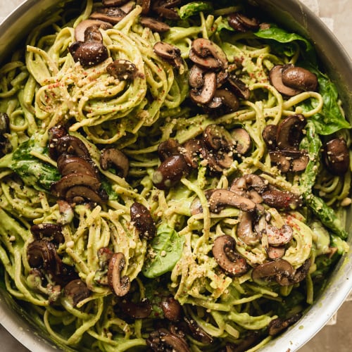 spinach and mushroom pasta in a stainless steel skillet. The pasta is creamy and pale green and topped with brown, sautéed mushrooms.