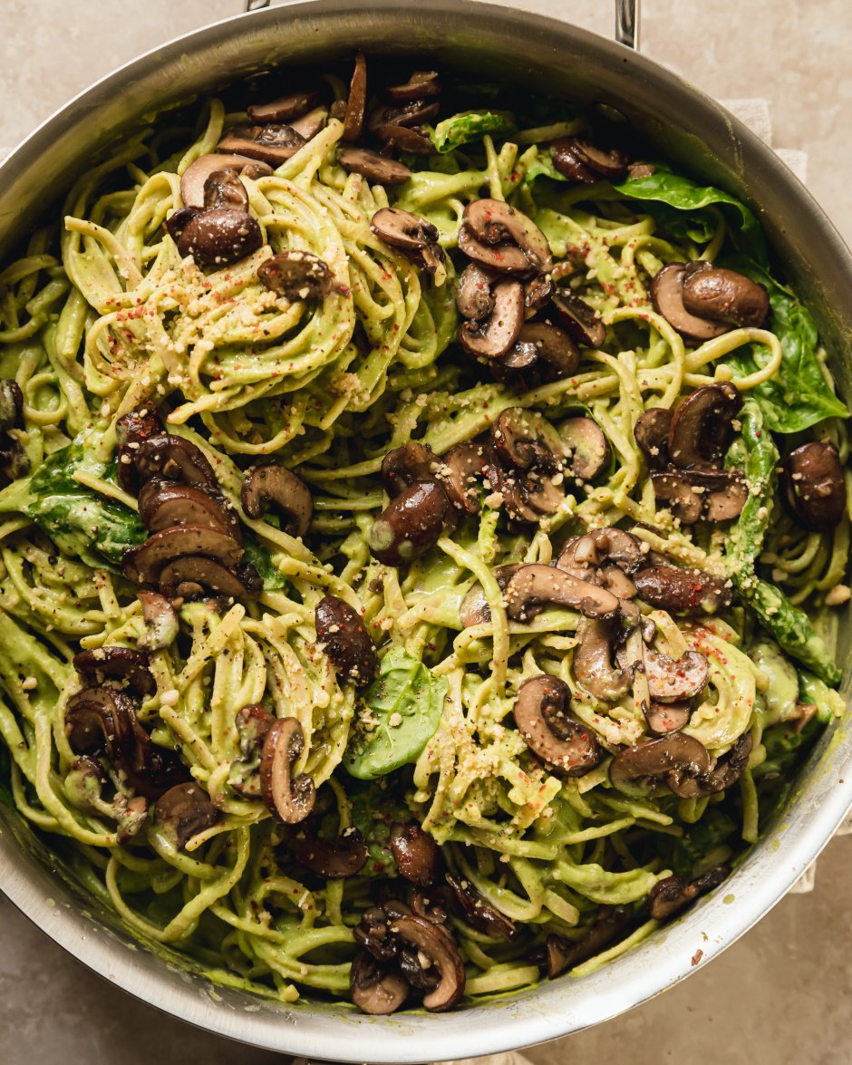 spinach and mushroom pasta in a stainless steel skillet. The pasta is creamy and pale green and topped with brown, sautéed mushrooms.