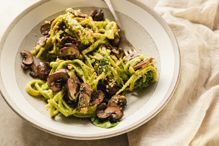 A 3/4 angle shot of a pale green sauced linguine in a grey bowl that's topped with sautéed mushrooms.
