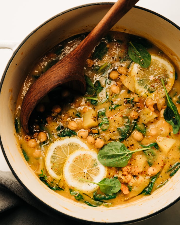An overhead shot of a creamy and thick lemony chickpea soup with spinach and potatoes. A wooden ladle is sticking out of the pot.
