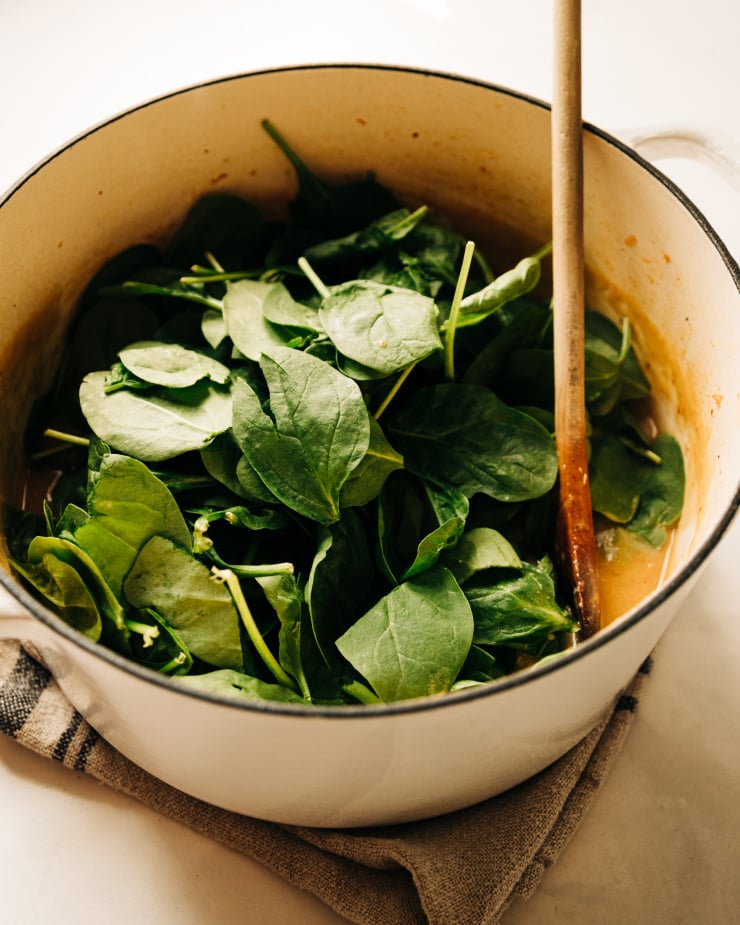 A 3/4 angle shot of a pile of baby spinach in a dutch oven style pot, on top of a soup.