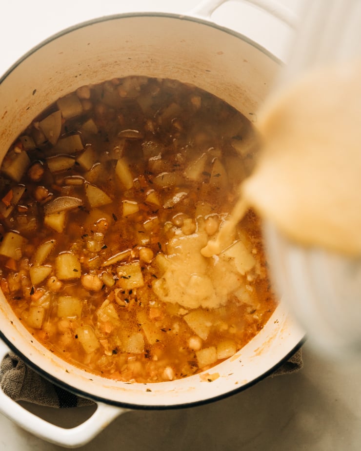 An overhead shot of a puréed portion of soup being poured back into a dutch oven-style pot.