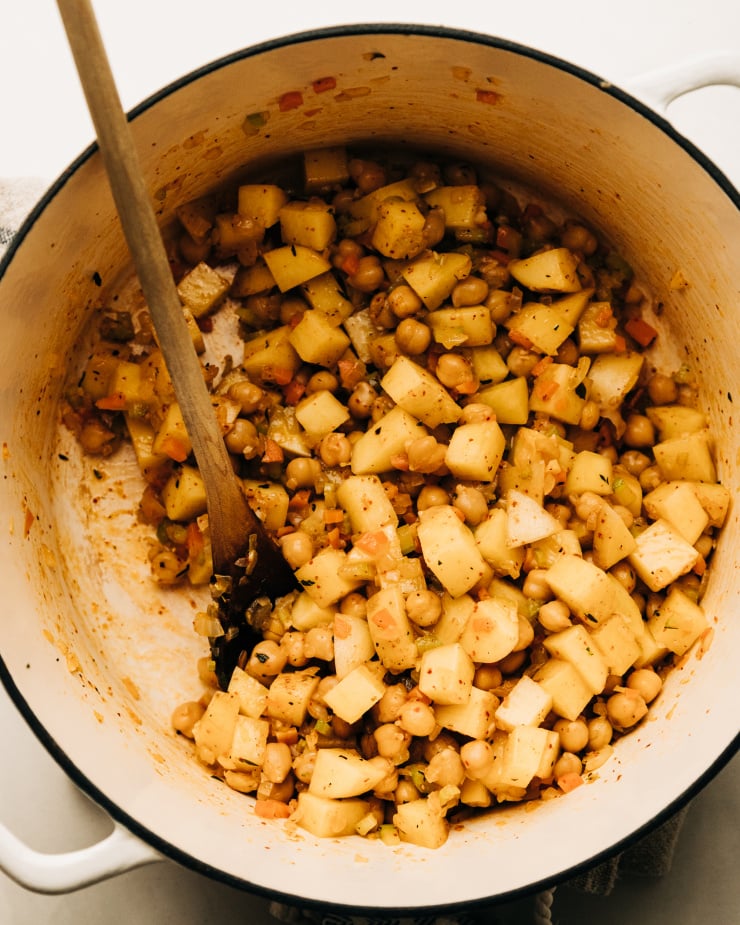 An overhead shot of sautéed chickpeas and potatoes in a white dutch oven-style pot.