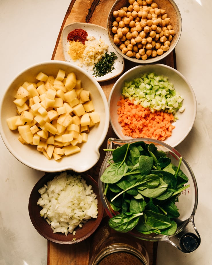 An overhead shot of prepped and chopped ingredients including celery, carrots, onions, baby spinach, minced garlic, thyme, and more,