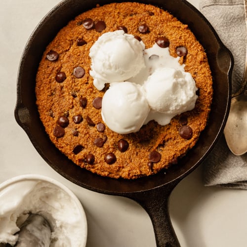 An up overhead shot of a slightly orange pumpkin chocolate chip skillet cookie topped with 3 scoops of vanilla ice cream.