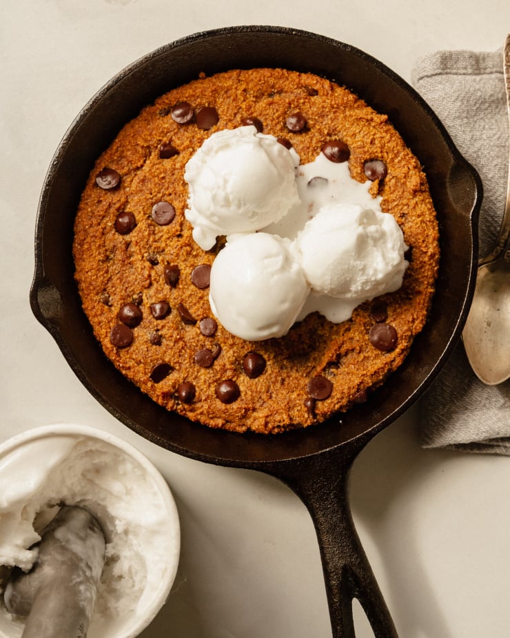 An up overhead shot of a slightly orange pumpkin chocolate chip skillet cookie topped with 3 scoops of vanilla ice cream.