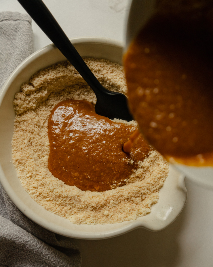A deep orange liquid mixture is being poured into a bowl with an almond flour mixture.