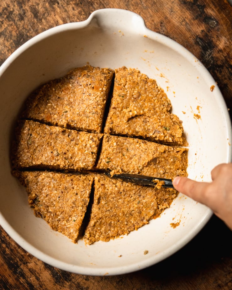 A hand is using a spatula to divide portions of veggie burger mixture in a mixing bowl.