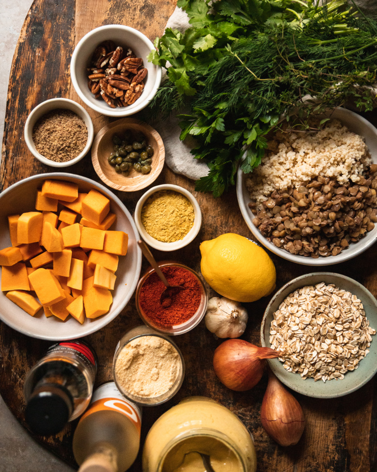 An overhead shot of ingredients used for vegan squash patties with mixed herb salsa verde, all on top of a worn wood cutting board.