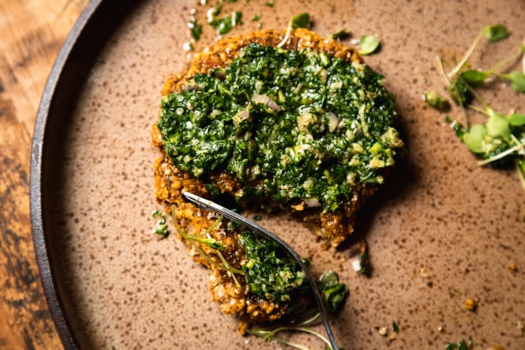 An up close, overhead shot of a vegan squash patty topped with mixed herb salsa verde. A fork is pulling away a bite.