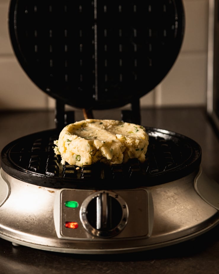 A head on shot of a portion of waffle mix inside of a heated and open waffle iron on top of a dark grey countertop.