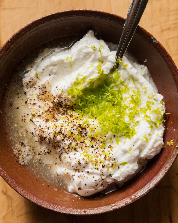 An overhead shot of vegan lime yogurt sauce ingredients in a brown bowl, before mixing together.