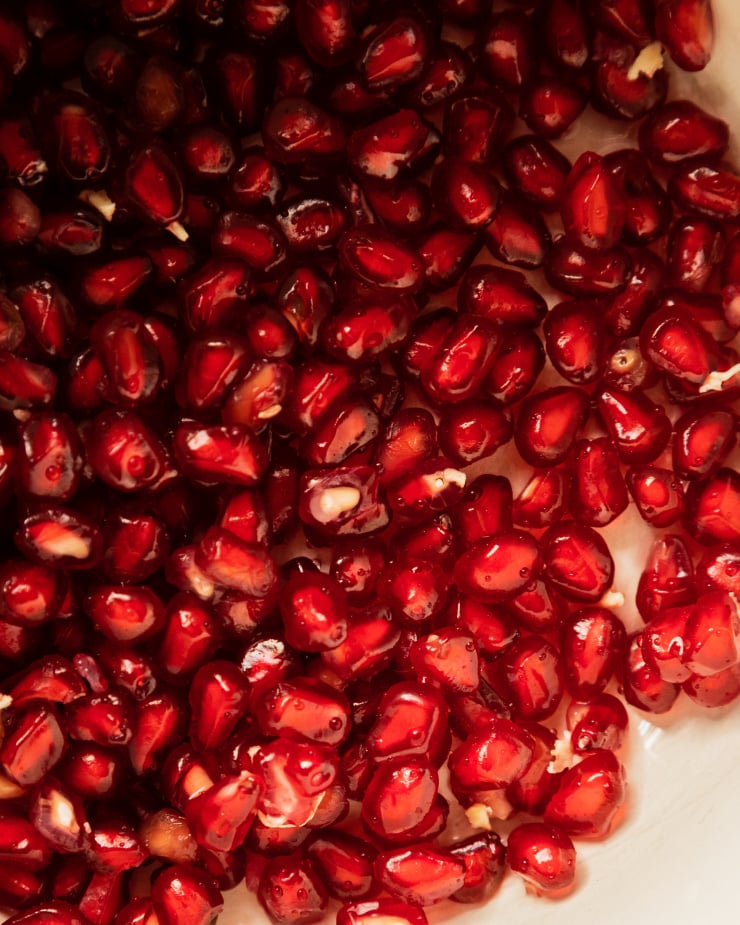 An up close, overhead shot of pomegranate arils in a white bowl.