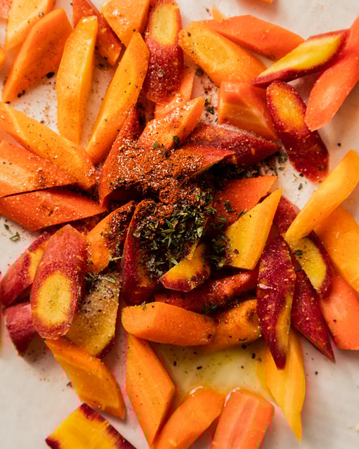 An up close, overhead shot of some chopped carrots topped with minced fresh thyme and smoked paprika, before being roasted in the oven.