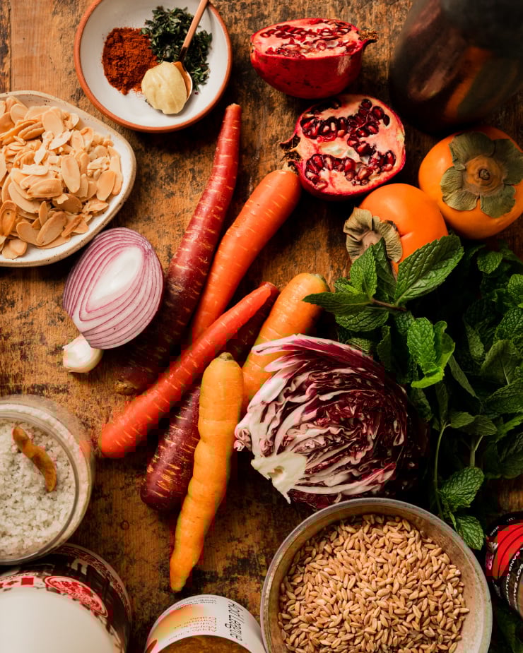 An overhead shot of whole ingredients for a holiday farro salad on top of a worn wood cutting board.
