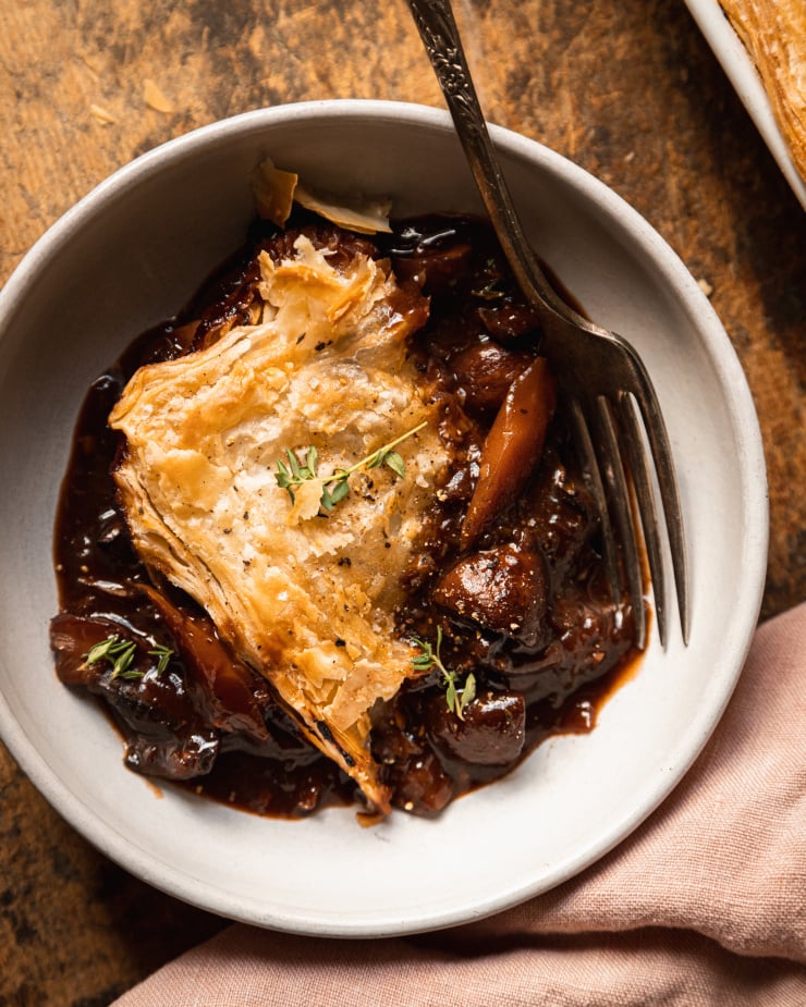 An up close, overhead shot of a single serving of vegan mushroom bourguignon pot pie topped with a crispy triangle of golden puff pastry.