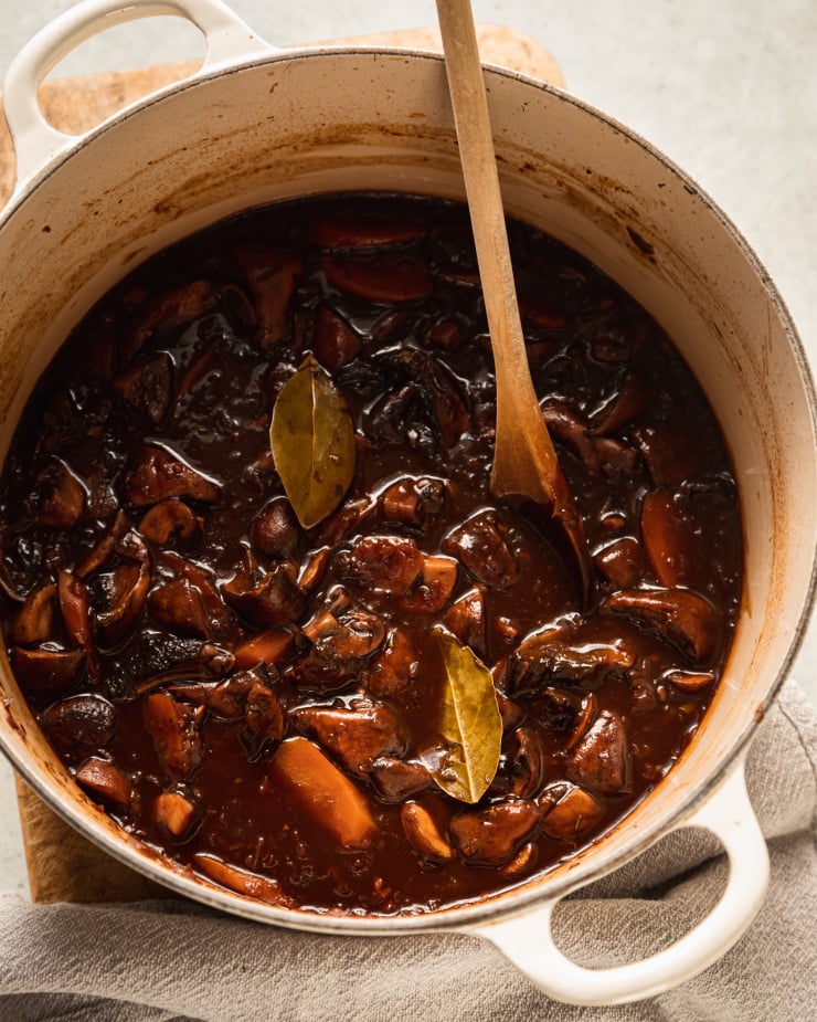 An overhead shot of a deep brown/almost burgundy vegan mushroom bourguignon in a white Dutch oven-style pot.