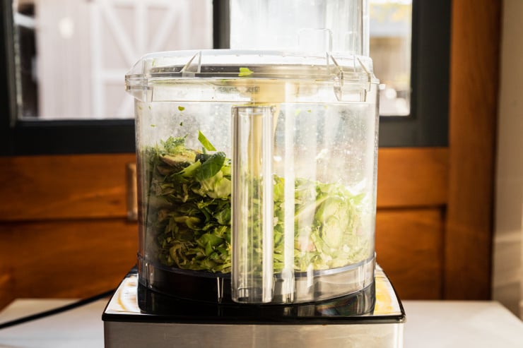 A head on shot of shredded brussels sprouts in a food processor. The bowl of the food processor is lit from behind.