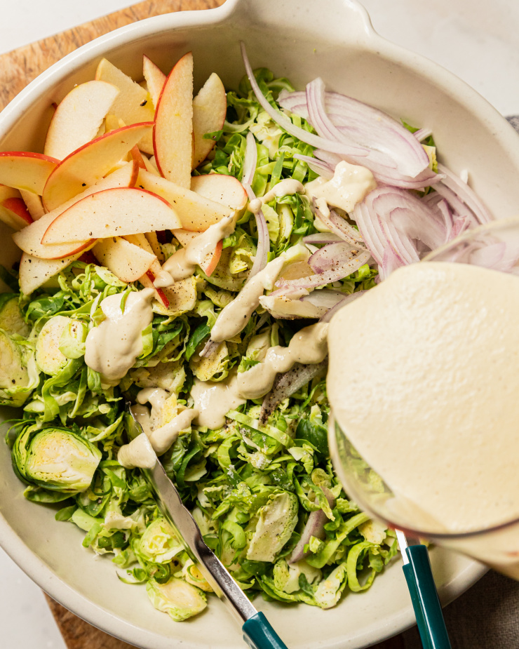 An overhead shot of creamy dressing being poured into a large bowl filled with salad.