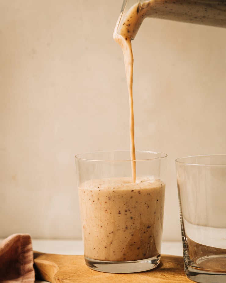 A head on shot of a flecked, creamy beige vanilla chip smoothie being poured into a clear glass.
