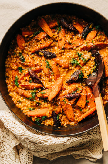 An overhead shot of barley risotto with roasted carrots in a black braiser-style pot.