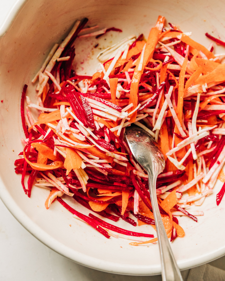 An overhead shot of a root vegetable slaw coming together in an off-white bowl.