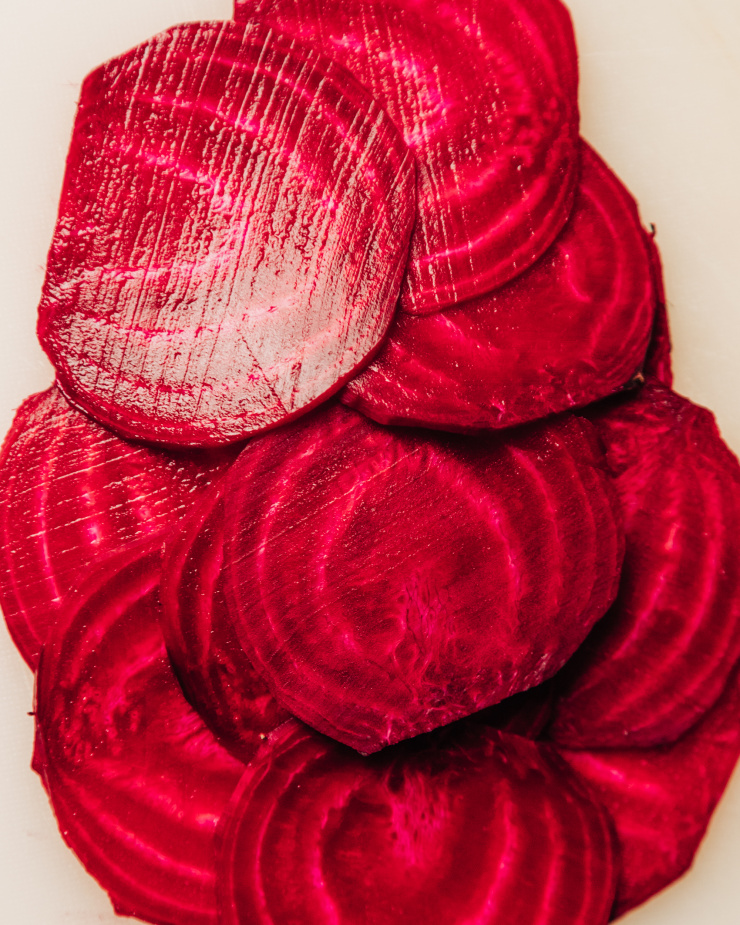 An up close, overhead shot of thinly sliced red beet. The slices are "shingled" over each other in layers.