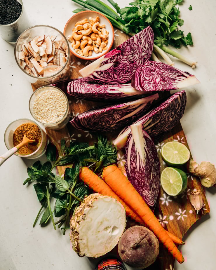 An overhead shot of ingredients for a cabbage side dish that is topped with a ginger lime root slaw, cashews, coconut, and sesame seeds.