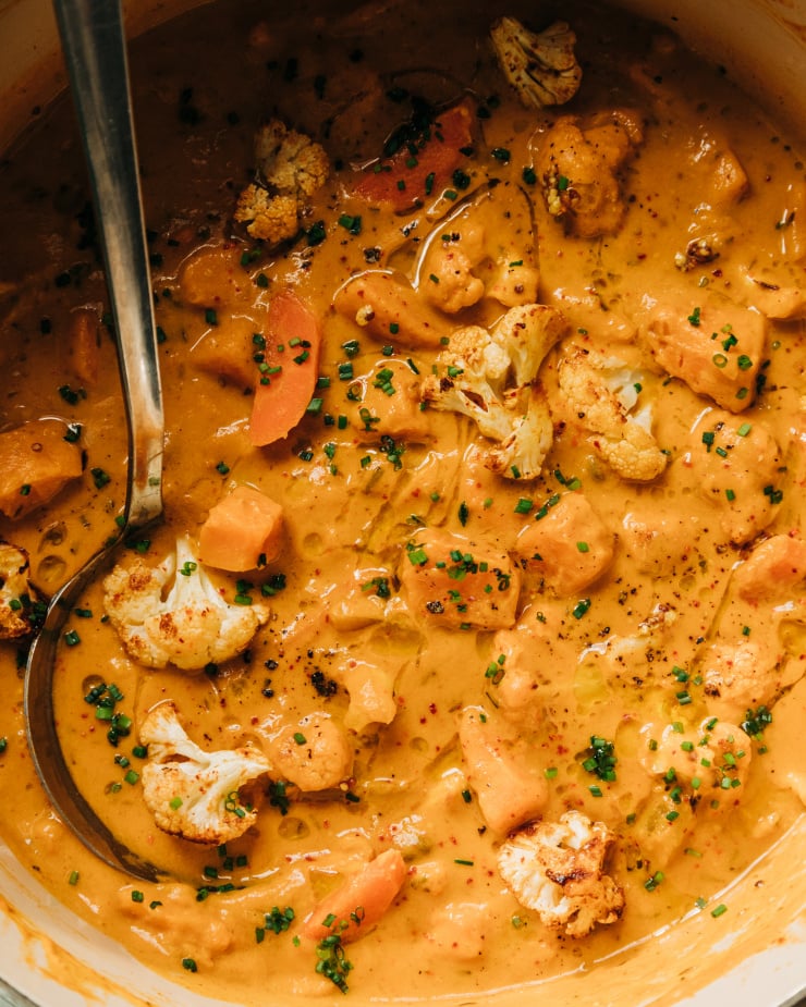 An up close, overhead shot of a creamy orange stew with sweet potatoes and cauliflower. The stew is garnished with chopped chives.