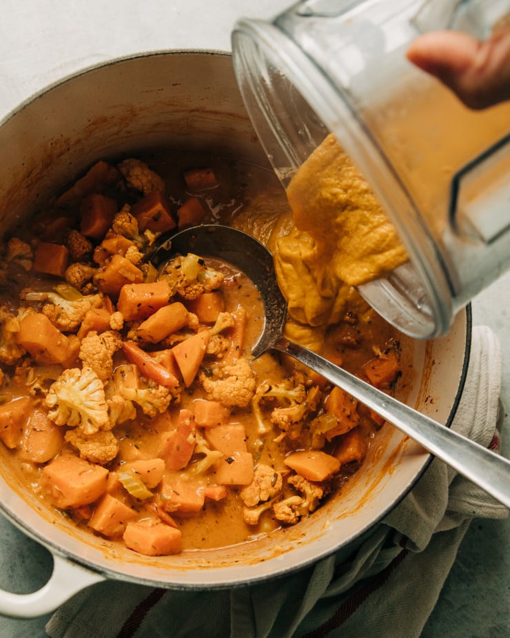An overhead image of a puréed portion of soup being poured back into a pot with whole components of the soup.
